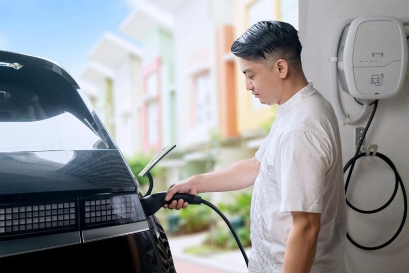 Man charging electric car in home garage